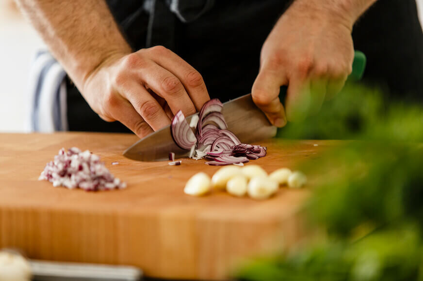 Close up of a chef cutting an onion on a wooden cutting board