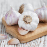 four heads of garlic sitting on a wooden board