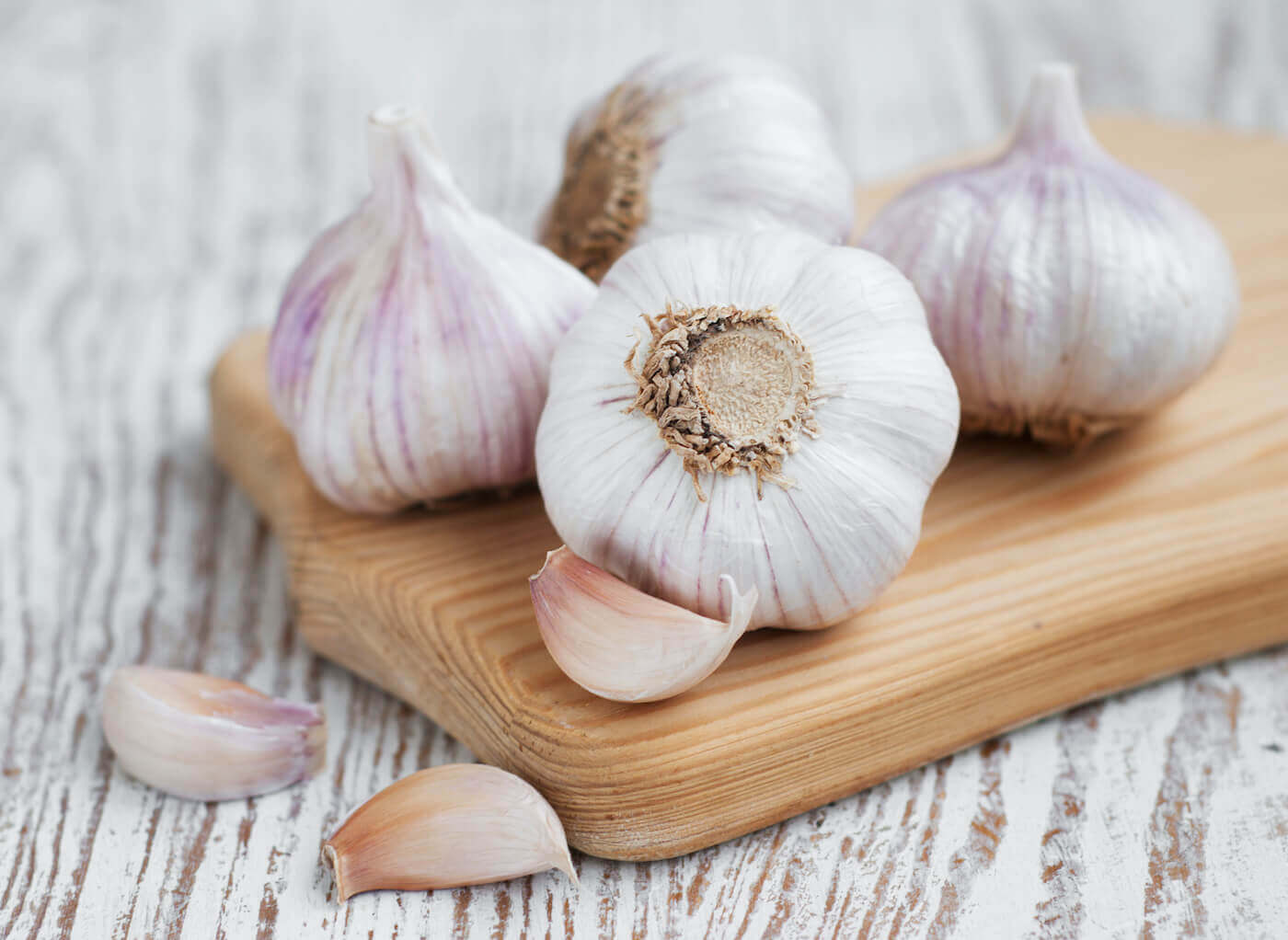 four heads of garlic sitting on a wooden board