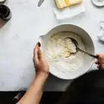 Hands mixing flour and butter in a ceramic bowl.
