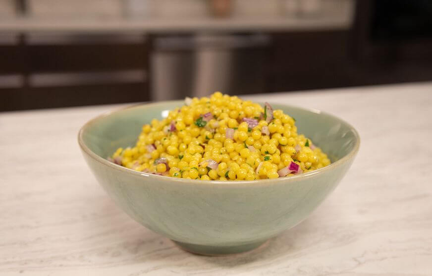 Yellow Israeli couscous in a light green bowl