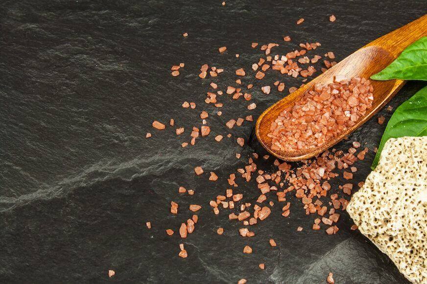 A large wooden spoon or paddle with Hawaiian alaea salt setting on a black countertop.