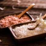 A pair of rectangular wooden bowls, one filled with coarse pink salt and another filled with coarse white salt.