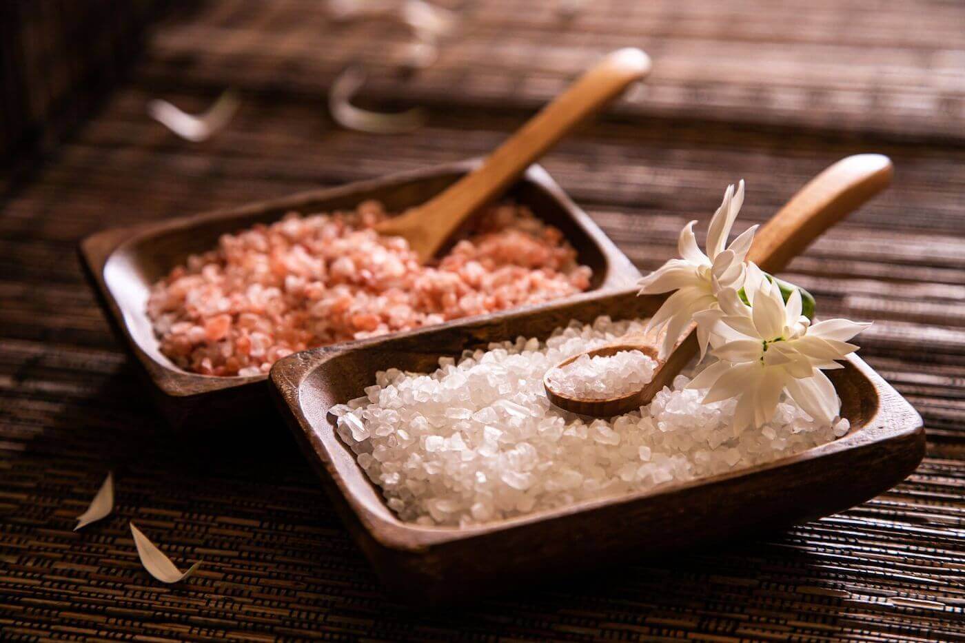 A pair of rectangular wooden bowls, one filled with coarse pink salt and another filled with coarse white salt.