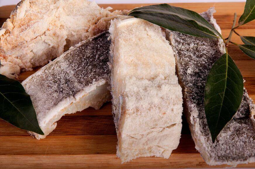 Irisan ikan cod asin diletakkan di atas talenan kayu.