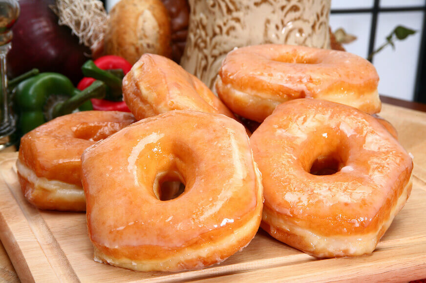 Glazed yeast doughnuts piled on a wooden cutting board