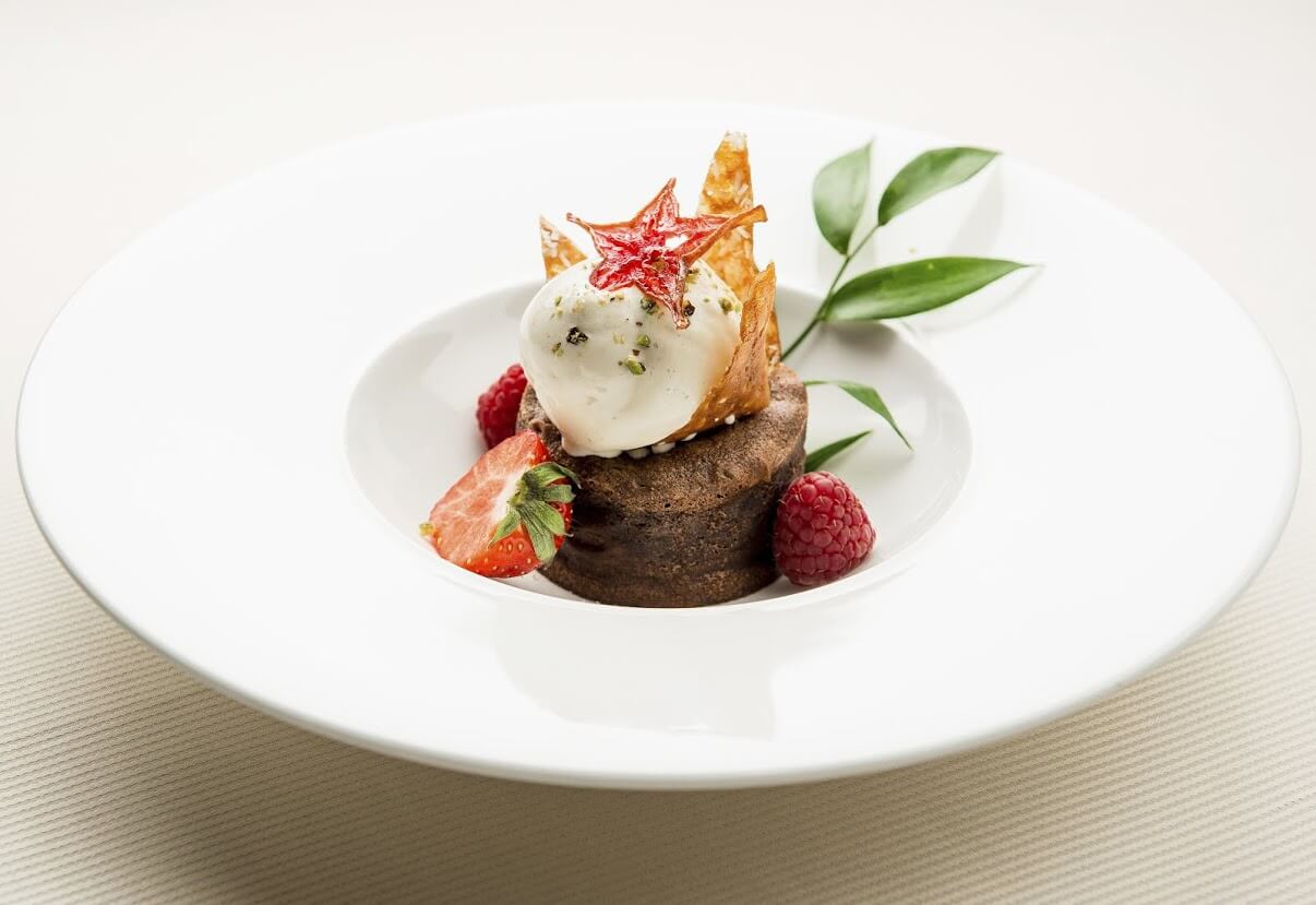 A finely plated dessert on a white plate with strawberry and raspberry