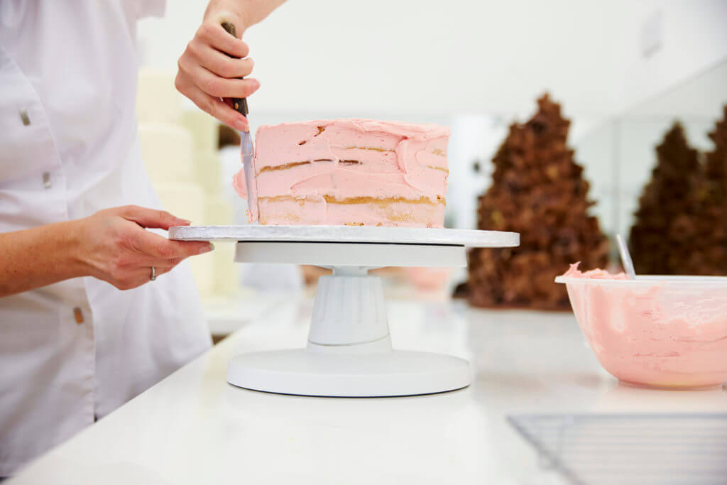 Pastry chef putting pink icing on a cake