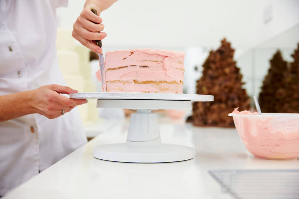 Pâtissier mettant du glaçage rose sur un gâteau