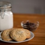 Chocolate Chip Cookies sitting on a plate in front of a jar of flour