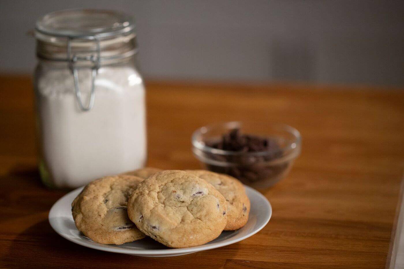 Chocolate Chip Cookies sitting on a plate in front of a jar of flour