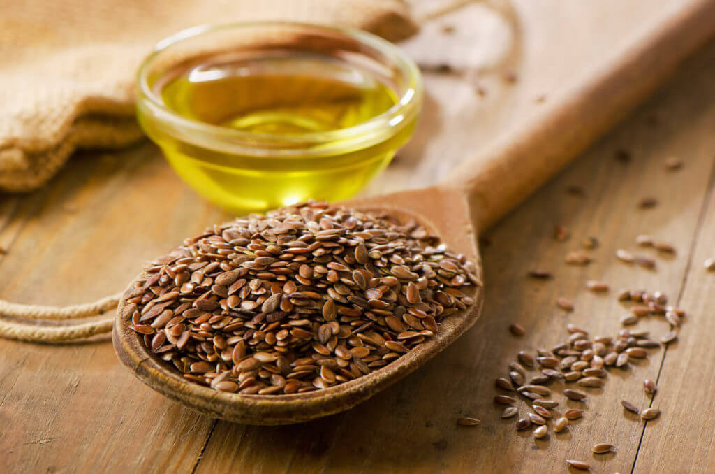 Brown flax seeds on a spoon with bowl of flaxseed oil