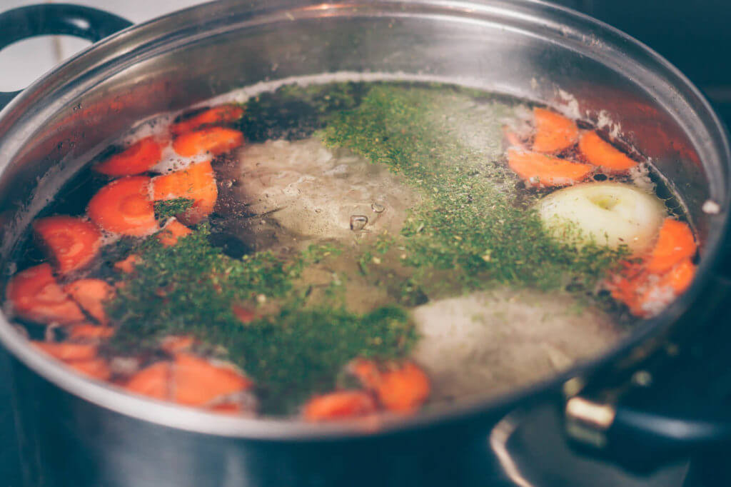 Cook boils vegetable broth in a saucepan on the stove