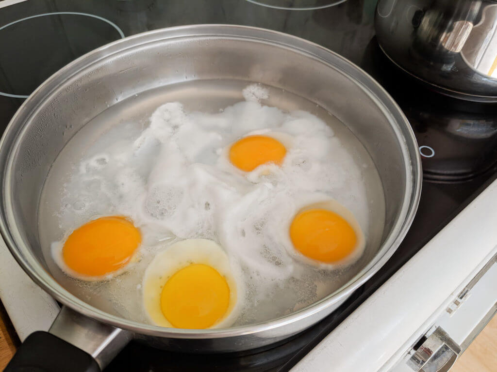 Poaching four fresh eggs in a pan of water until partially cooked