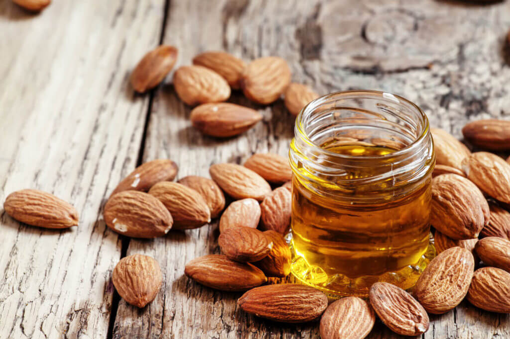 Sweet Almond Oil, first extraction, in a small glass jar, surrounded by almonds