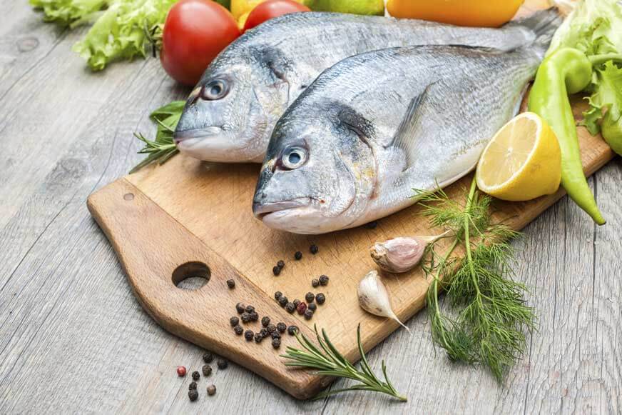 Fresh raw fish gilthead bream on wooden cutting board with herbs