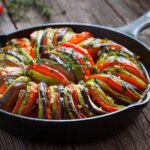Vegetable ratatouille baked in cast iron frying pan on vintage wooden table
