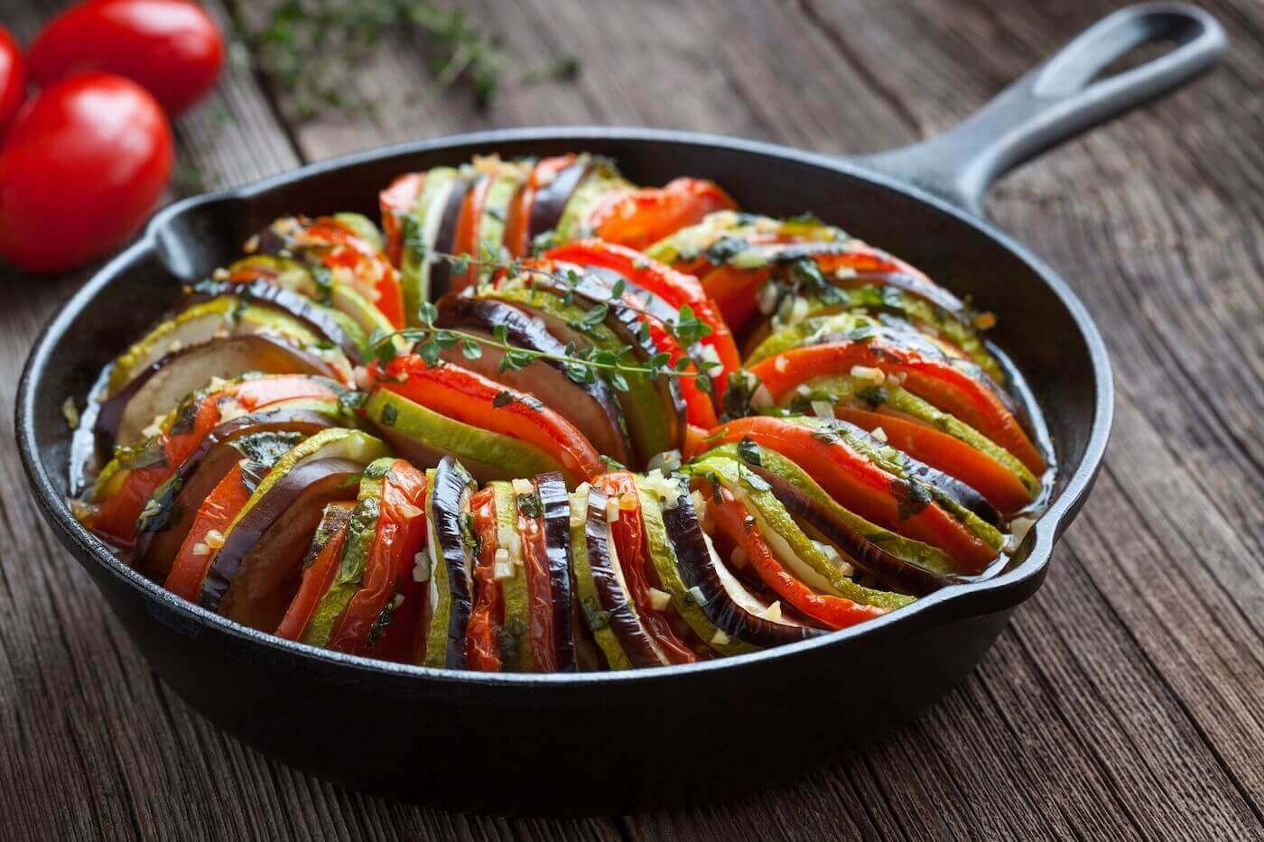 Vegetable ratatouille baked in cast iron frying pan on vintage wooden table