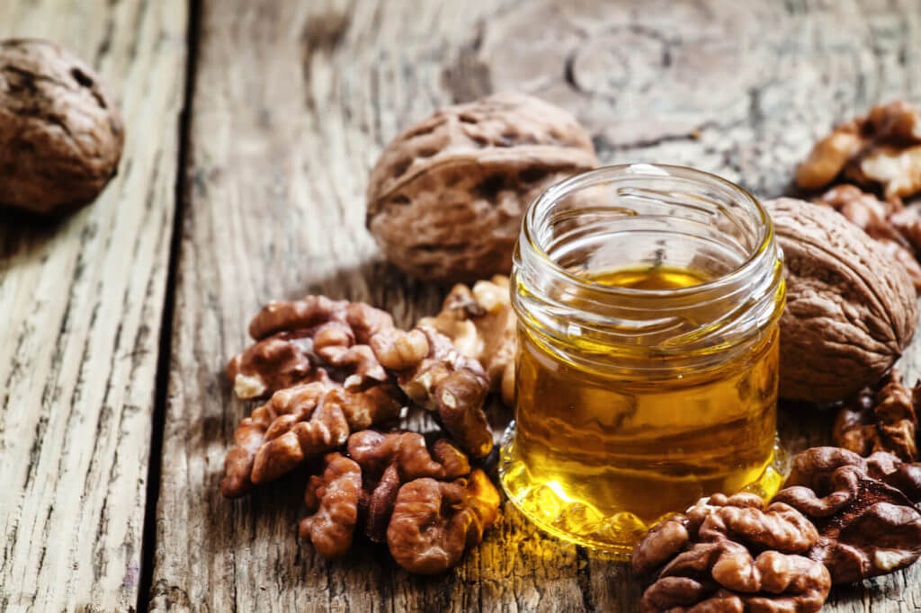 Walnut oil in a small jar and kernels on old wooden background