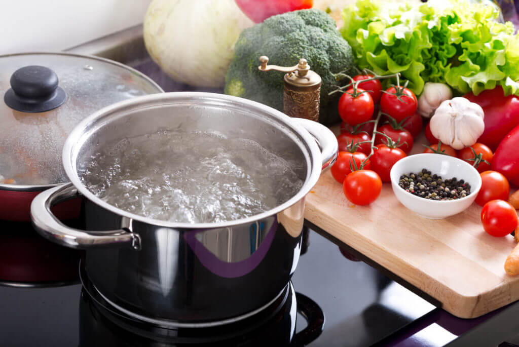 boiling water in a cooking pot on the cooker next to tomatoes and other vegetables