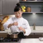 Chef in uniform stirring sauce in a small bowl above the stove