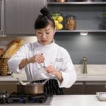 Chef in uniform stirring sauce in a small bowl above the stove