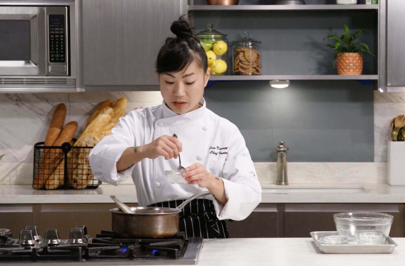 Chef in uniform stirring sauce in a small bowl above the stove