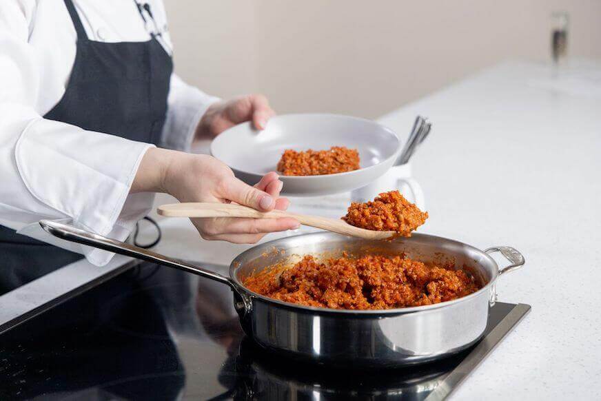 Chef spooning ragu alla bolognese into a bowl