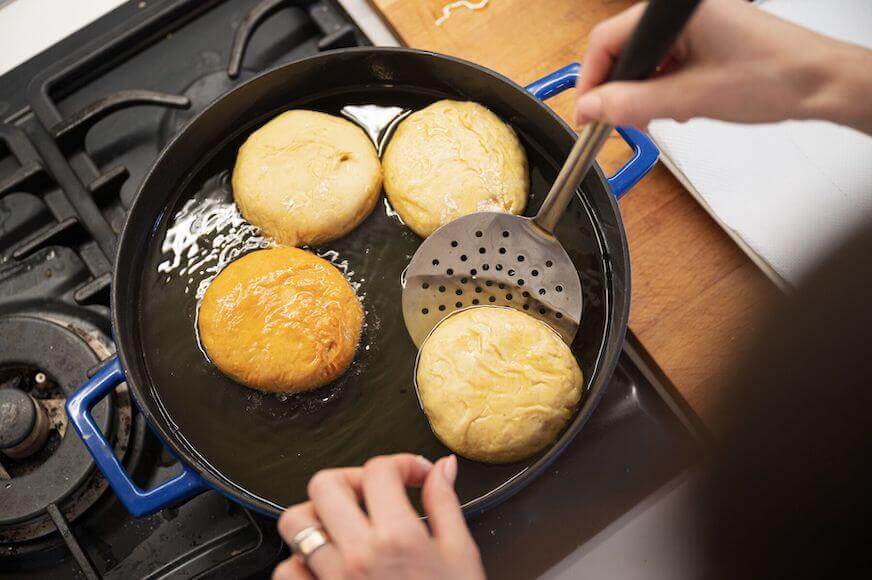 Top view of hand turning over vegan donuts as they fry in the hot oil