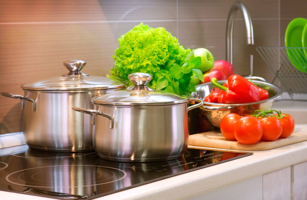 Metal pots, tomatoes, peppers and green vegetables on a stove