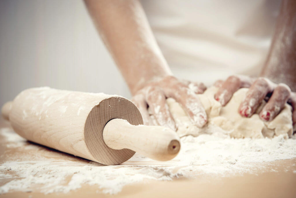 Wooden rolling pin next to chef kneading dough
