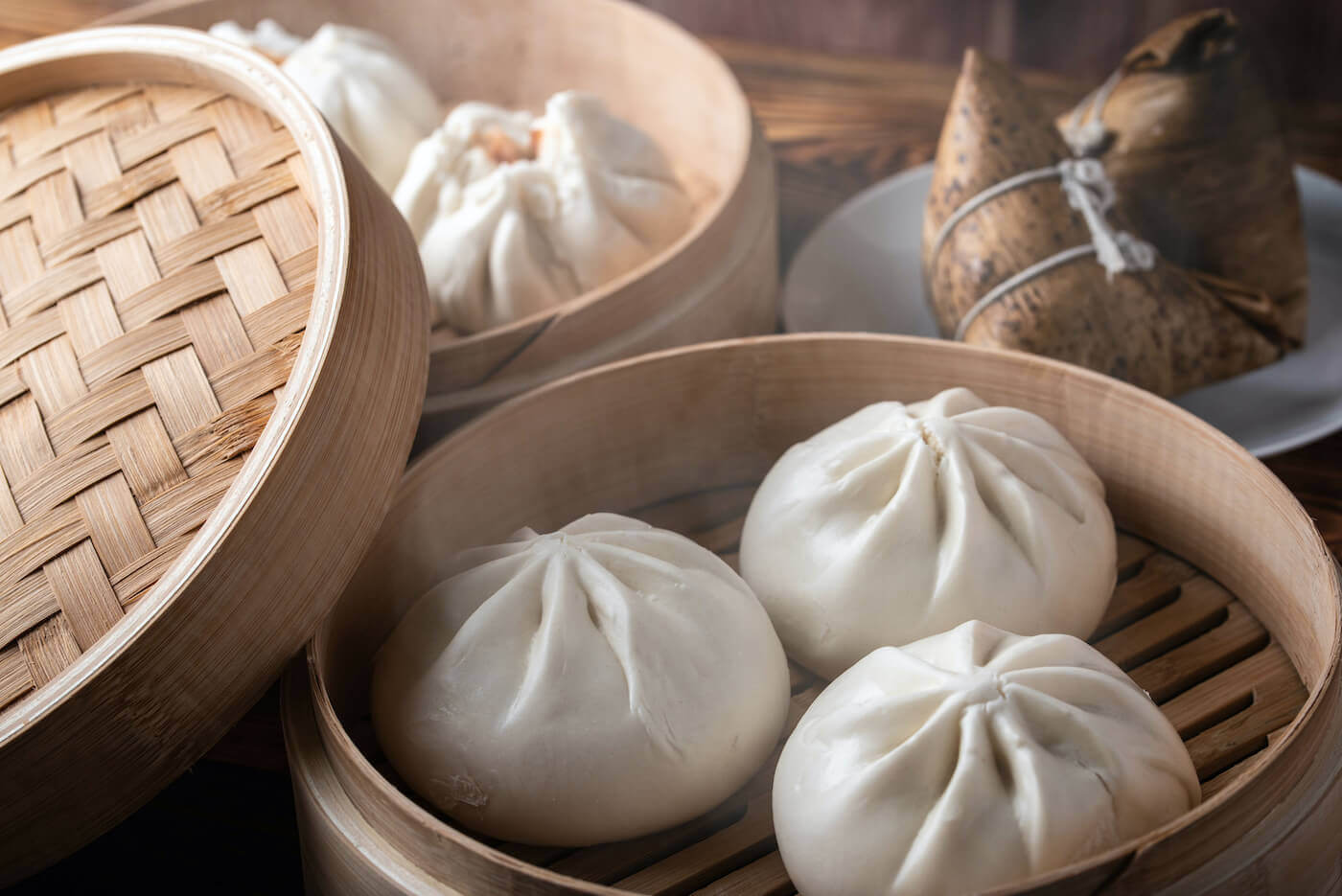 Three steamed bao buns sit in a small wooden basket.