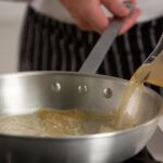 Chef pouring stock into a silver pan