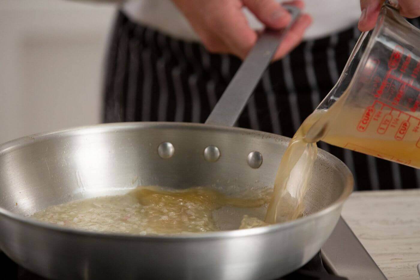 Chef pouring stock into a silver pan