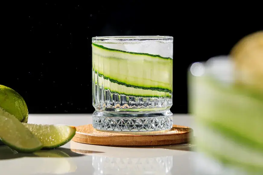 Cucumber ribbon cocktail with lime wedges on the side, served in a clear tumbler glass.