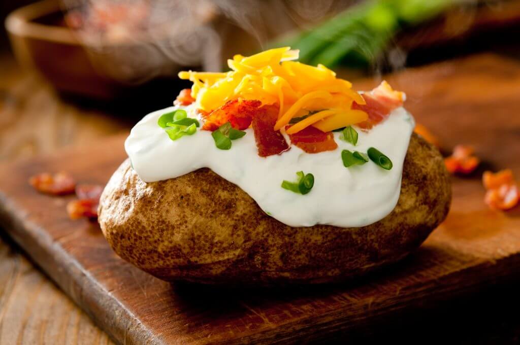Closeup of a hot baked potato topped with sour cream, bacon, green onions and cheddar cheese.