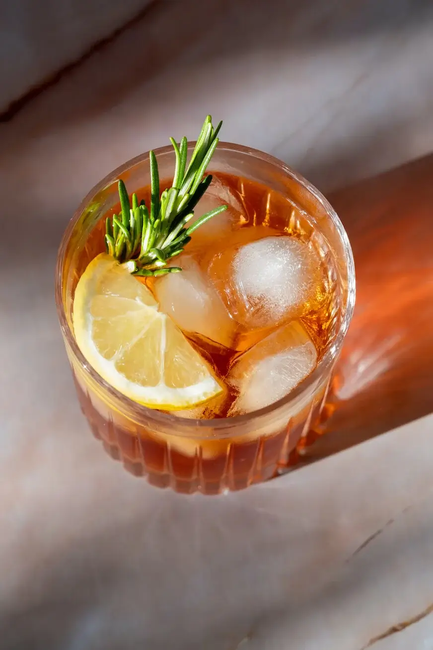 Top-down view of a cocktail with ice, lemon slice, and rosemary sprig in a clear glass.