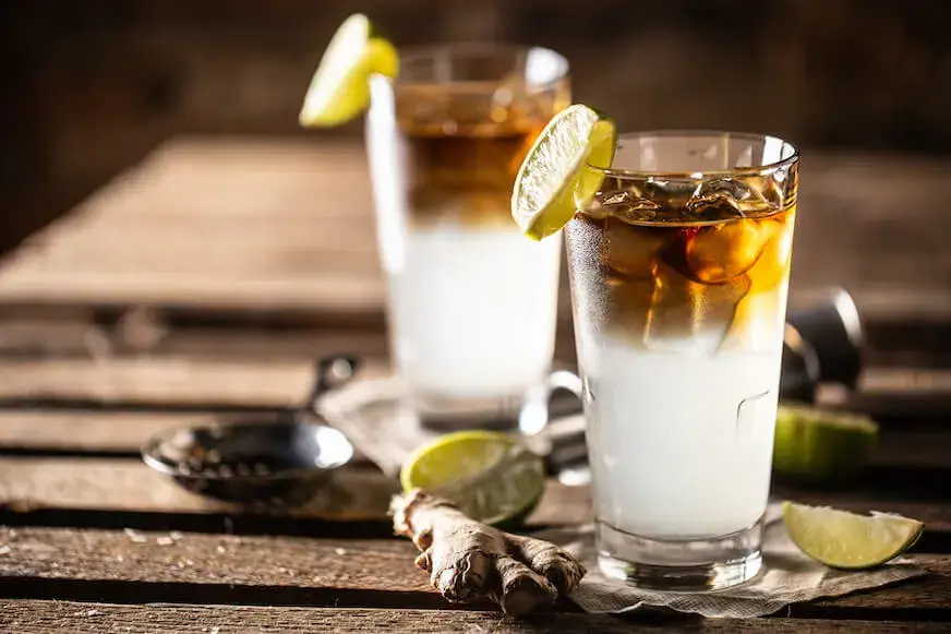 Two Dark and Stormy cocktails with lime wedges and visible layers of dark rum and ginger beer.