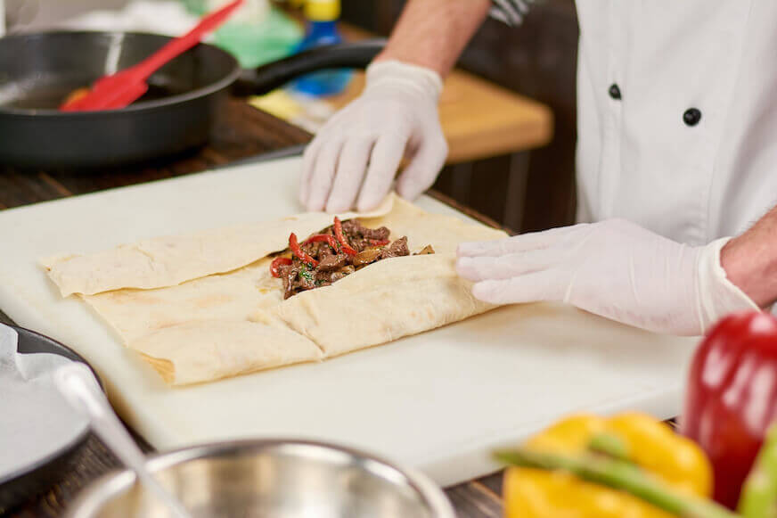 Chefs hands rolling a burrito with beef and peppers