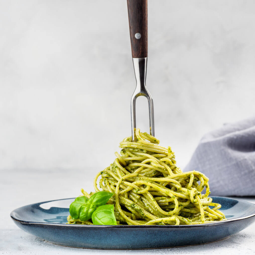 Spaghetti pasta with pesto on a blue plate and with a fork for twisting in the middle