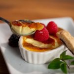 A spoonful of creme brulee with plated dessert in the background