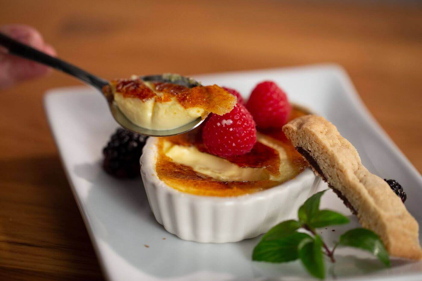 A spoonful of creme brulee with plated dessert in the background