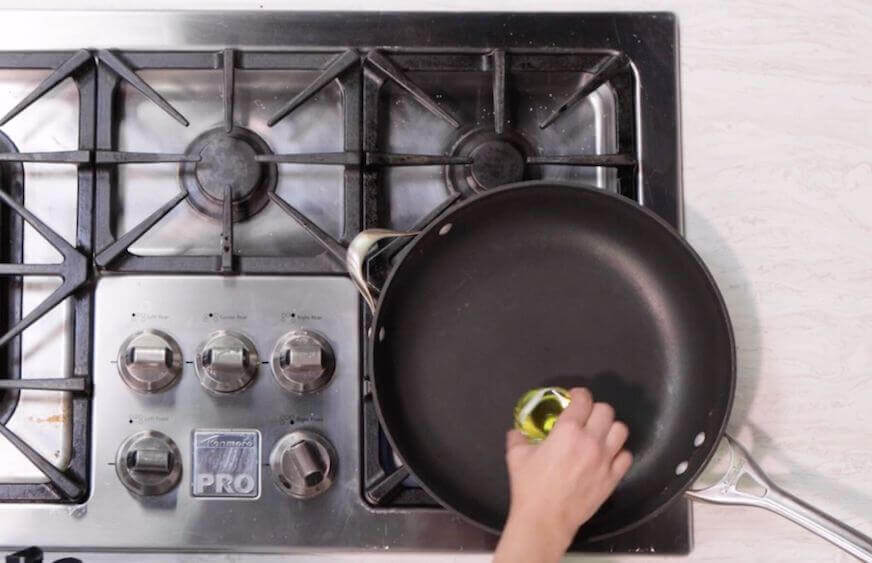 Chef pouring oil into a skillet on the stove