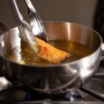 Tongs frying an egg roll in a silver pot