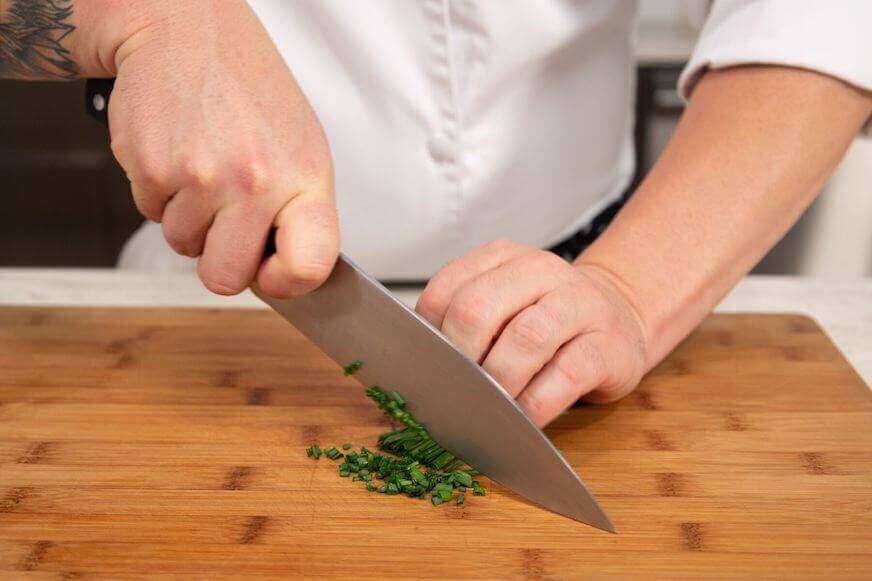 Chef chopping chives on a wood cutting board