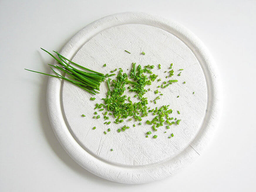 Image of chive shoots on a chopping block, partially minced.