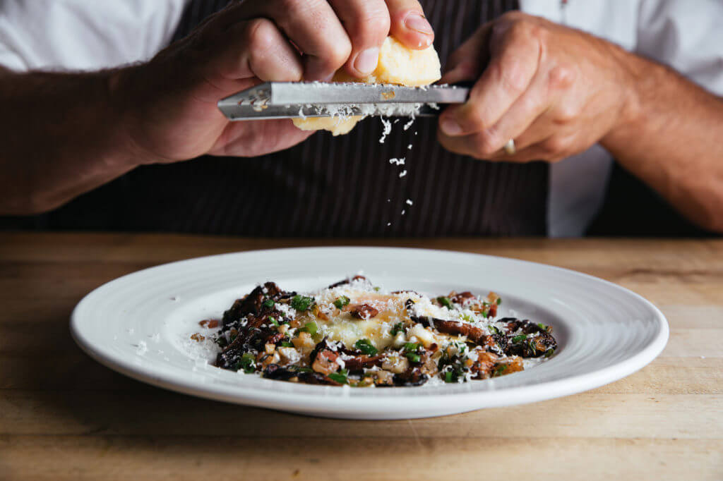 Chef grating cheese over a white plate