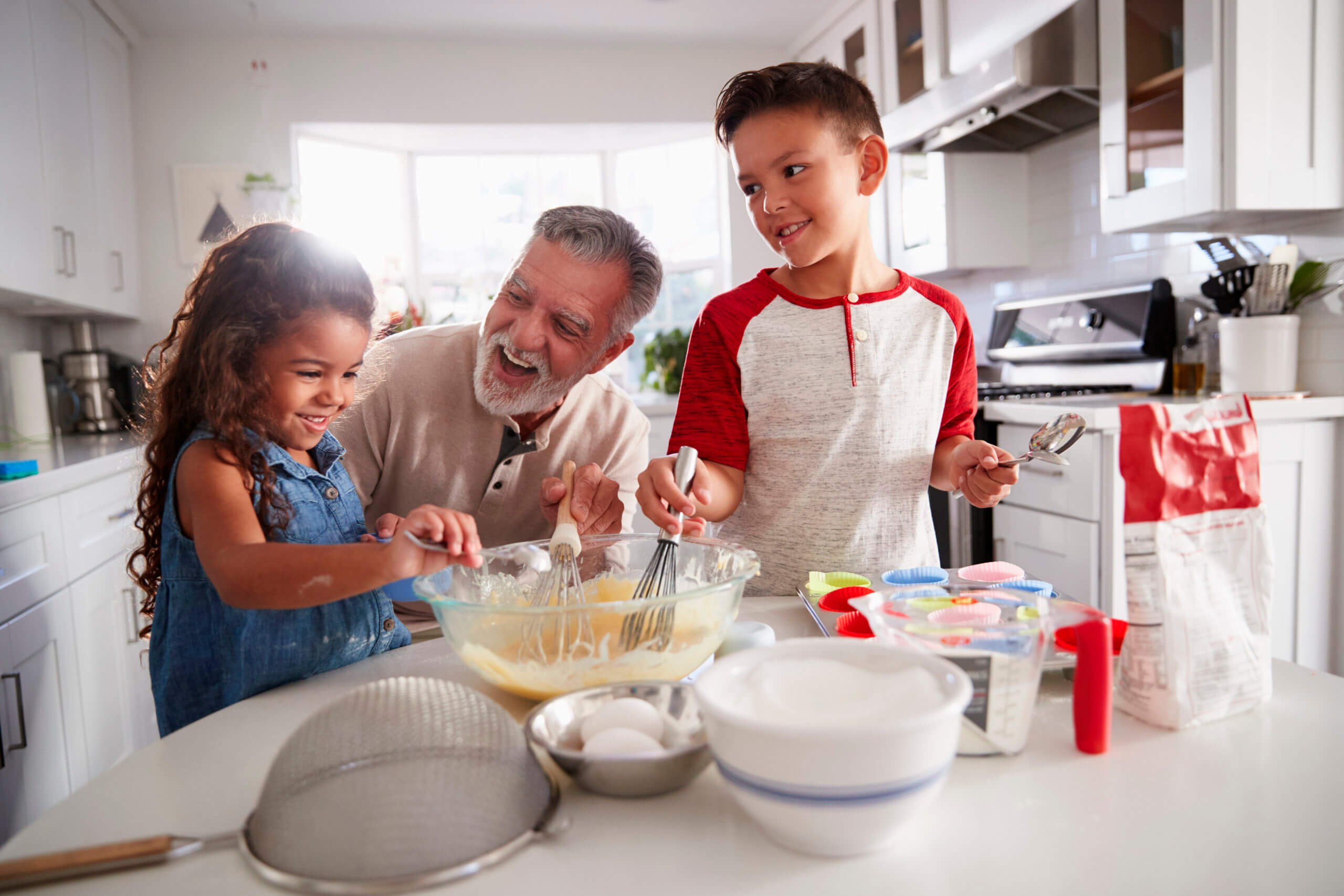 Brother and sister standing at the kitchen table making cake mix with their grandfather, close up