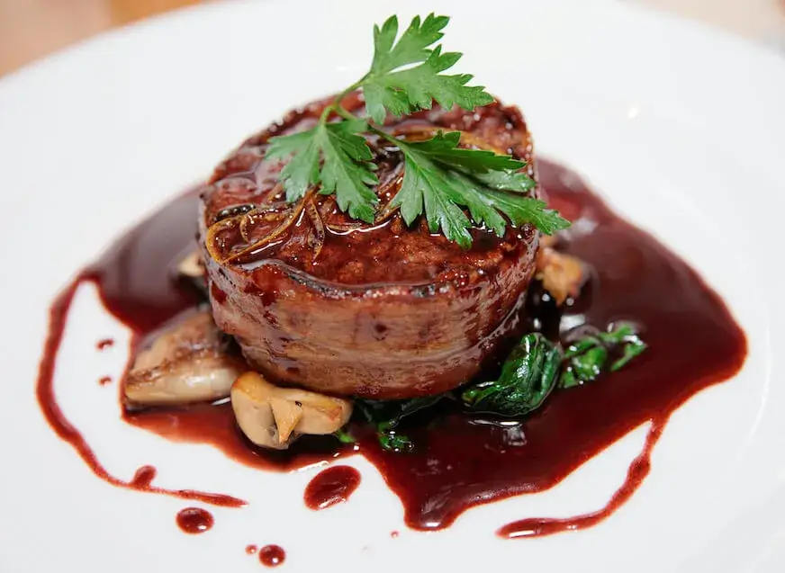 Plated filet mignon topped with parsley and surrounded by a glossy red wine demi-glace made from Espagnole sauce.