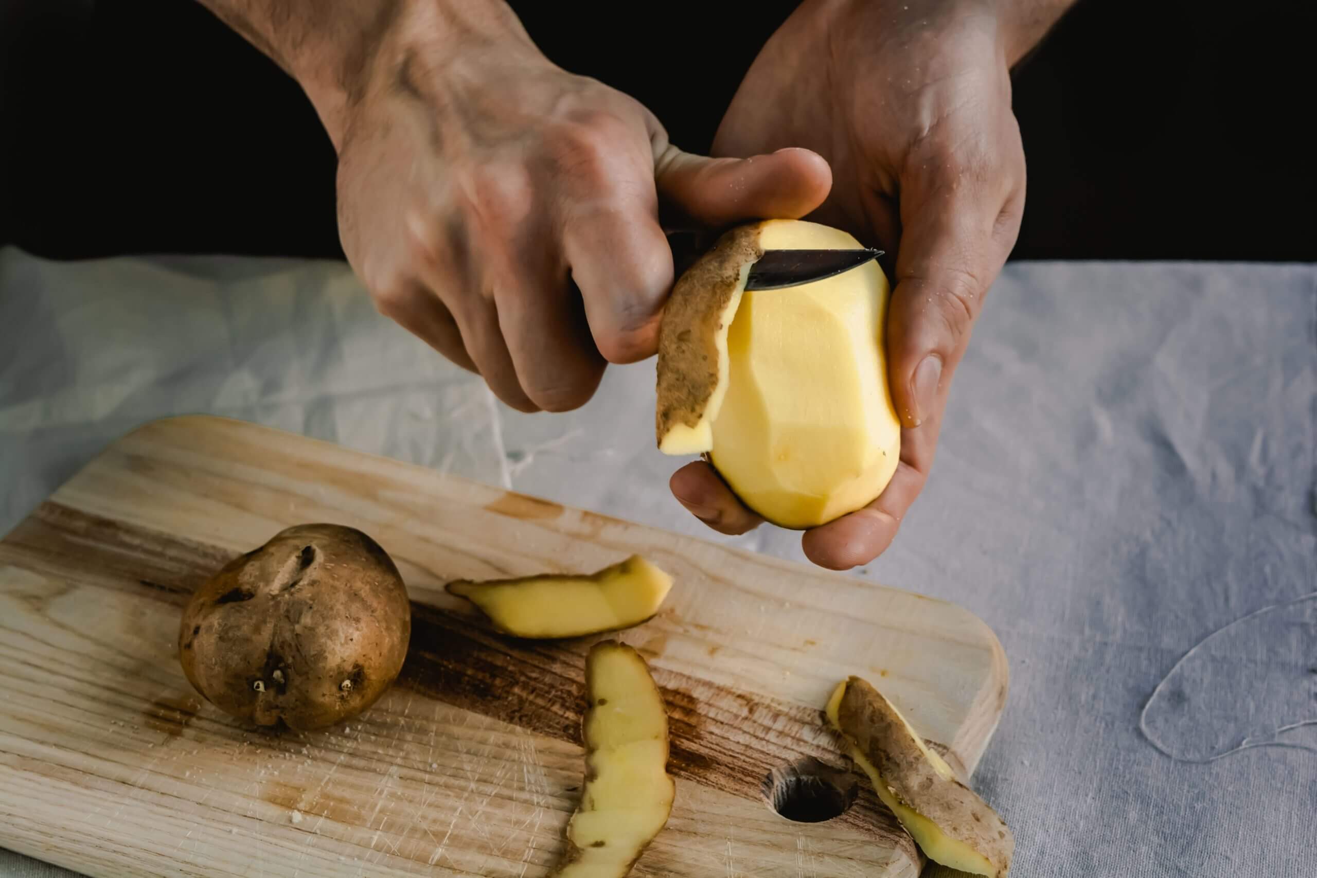 Chef peeling potatoes on wooden cutting board